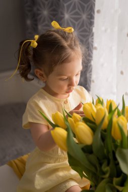 Bir buket sarı lalesi olan üzgün bir kız yana bakıyor. Tatil çocuğa mutluluk getirmez. Yas tutar. Bahar tatili için tebrikler sarı laleli çocuk.