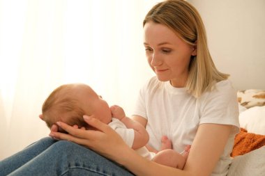 Anne kucağında yeni doğmuş bir bebek tutuyor. Arka planda güneş pencereden parlıyor..