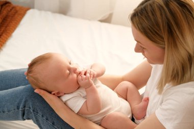 Anne kucağında yeni doğmuş bir bebek tutuyor. Arka planda güneş pencereden parlıyor..