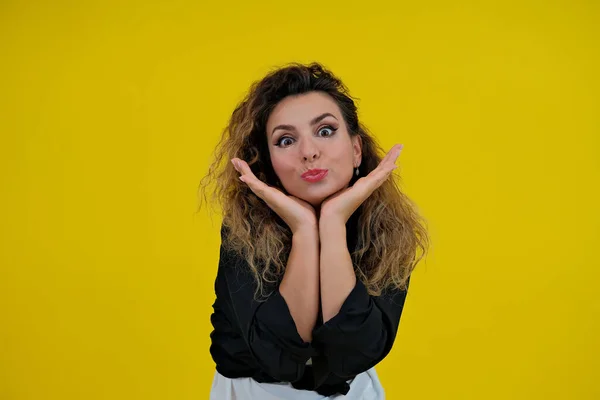 Wow. Close-up portrait of a beautiful girl on a yellow background. a woman holds her face with her hands, hands on her cheeks, isolated yellow wall. Shocked surprised stunned. positive human emotions