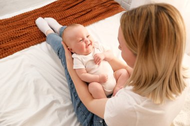 Anne kucağında yeni doğmuş bir bebek tutuyor. Arka planda güneş pencereden parlıyor..