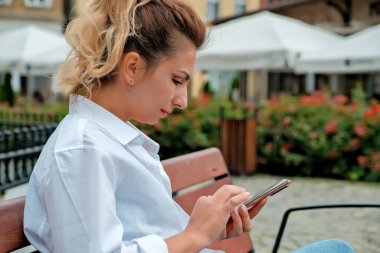 Güzel bir kız bankta oturuyor ve elinde bir telefon tutuyor. Kız telefonla yemek sipariş ediyor. Kız telefonda konuşuyor, gülüyor, mutlu, şaşırmış. .