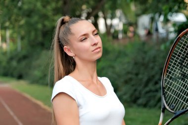 a girl in a white sports dress stands on a tennis court and holds a racket. portrait of a girl on the tennis court.