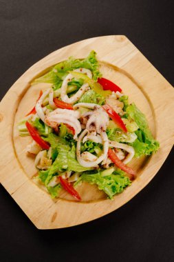 Tahta tabakta deniz ürünleri ve taze sebze salatası ve koyu bir arka plan. Karidesli salata, küçük ahtapot ve kalamar halkaları.