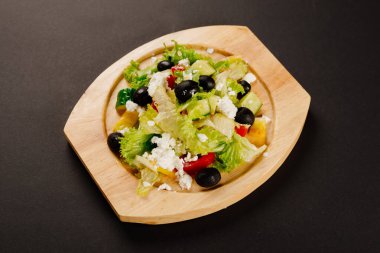 Siyah zeytinli Yunan salatası ve ahşap tabakta yumuşak peynir ve koyu arkaplan