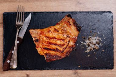 Pirzola üzerinde domuz bifteği bir tahta üzerinde, sebzeli pilavın yanında, baharatlı kaba tuz var.