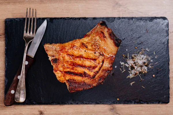 Pirzola üzerinde domuz bifteği bir tahta üzerinde, sebzeli pilavın yanında, baharatlı kaba tuz var.