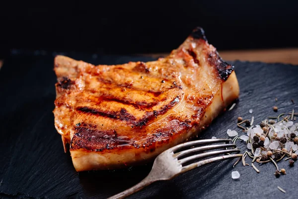 Pirzola üzerinde domuz bifteği bir tahta üzerinde, sebzeli pilavın yanında, baharatlı kaba tuz var.