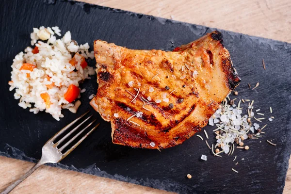 Pirzola üzerinde domuz bifteği bir tahta üzerinde, sebzeli pilavın yanında, baharatlı kaba tuz var.