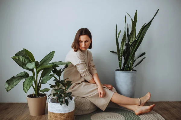 Mujer de mediana edad sentada en casa rodeada de plantas verdes domésticas — Foto de Stock