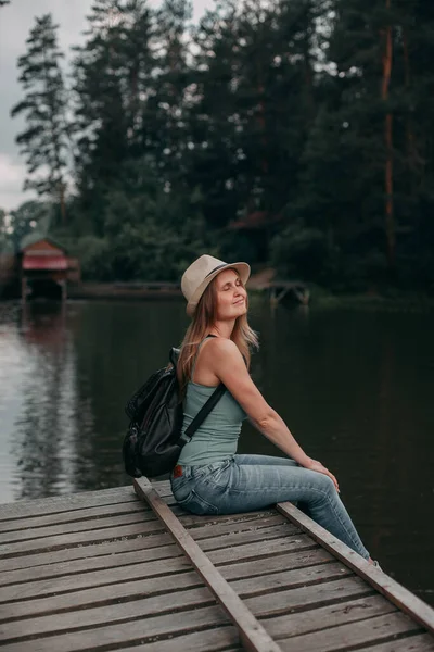 Niña en una parte superior azul de vacaciones en una caminata con una mochila junto al lago en la zona del bosque — Foto de Stock