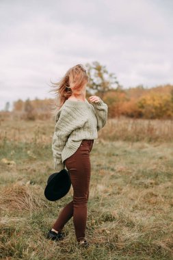 Sonbaharda bir tarlada yeşil kazak ve kahverengi kot giyen sarışın bir kızın portresi.