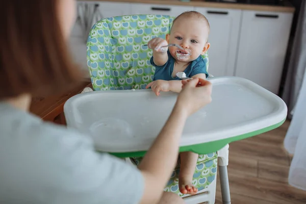 Mãe alimenta seu filho de um ano de idade na cozinha — Fotografia de Stock