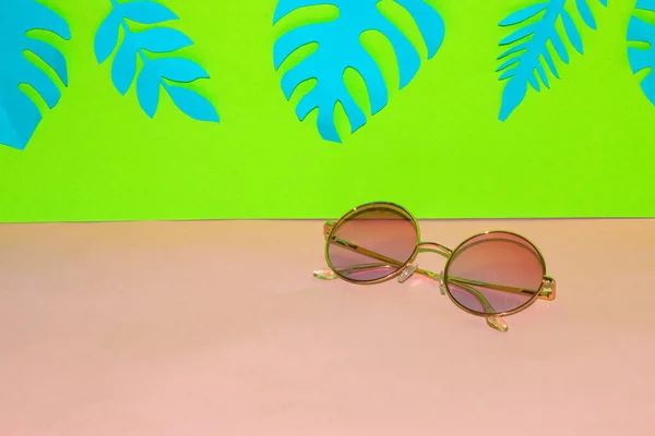 sunglasses on a pink green background, above the glasses jungle leaf, a creative summer concept