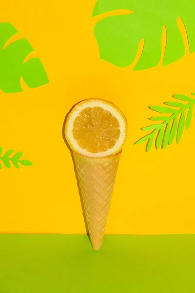 slice lemon in ice cream cone on yellow background with tropical jungle leaves, creative summer design, tropical vocation