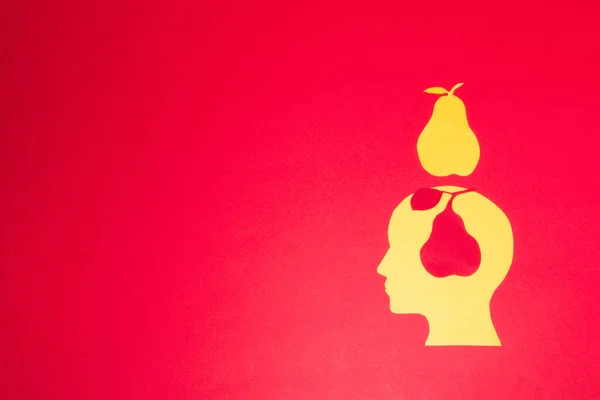 yellow paper head on red background with red pear in head and yellow above head, creative art design, copy space, minimal concept
