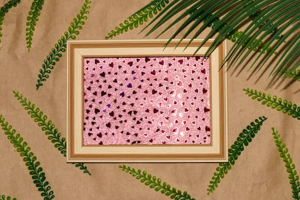wooden frame with glitter pink heart background as copy space, around the frame vintage background with jungle leaves, creative summer modern design, abstract background