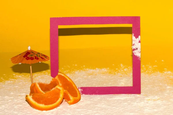 cyclamen color frame on yellow background with sand, creative summer concept, next to slice orange fruit and parasol frame, creative tropical design with copy space