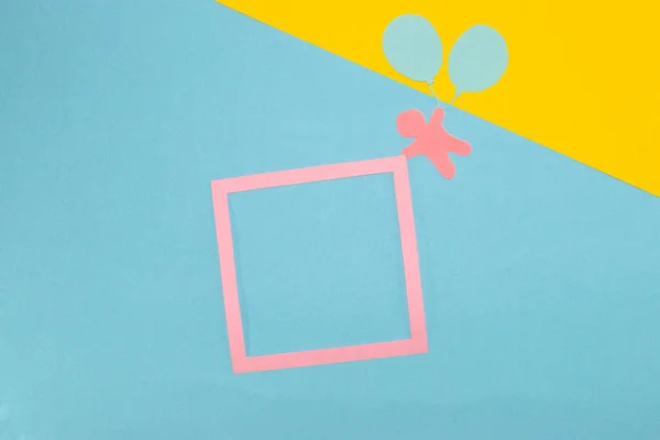 paper man flying paper balloons and holding pink frame as copy space on pastel blue-yellow background