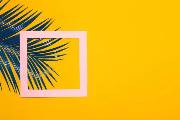 blue palm leaf with pink frame as copy space on the left side of the background in addition to a lot of copy space and product space, tropical design