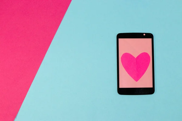 phone with pink screen and big pink heart on blue part pink-blue wallpaper, creative design, copy space, modern trendy idea