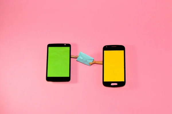 mobile phone with green screen delivers letter with yellow screen, hands it from hand to hand, pink background, copy space, creative idea, minimal concept