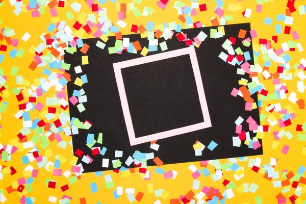 black paper with pink frame as copy space, around the paper yellow background with colorful chopped paper, creative party design