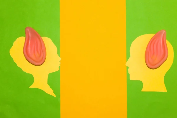 male and female paper heads looking at each other, have elf ears, creative art desgin have an ear for a person through the nose, listen, give a chance, minimal concept yellow-green background