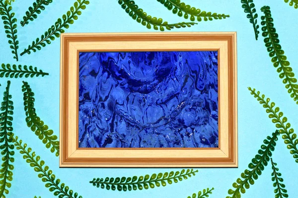 wooden frame with blue water as copy space, eye frame jungle leaves on pastel blue background, creative art modern design