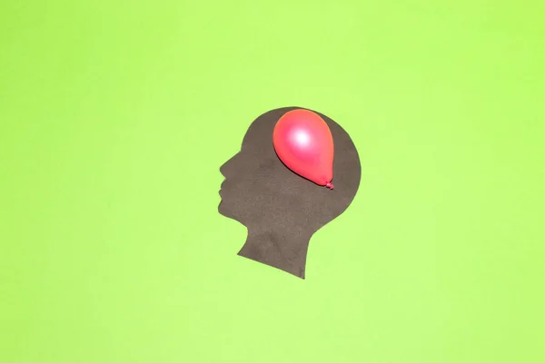 black paper head with red balloon instead of brain, green background creative art design