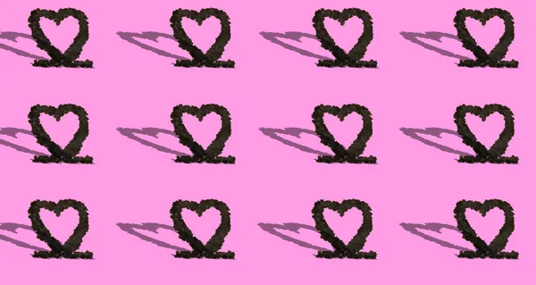 black hearts from black shredded paper copied all over pink background with shadows, creative love design