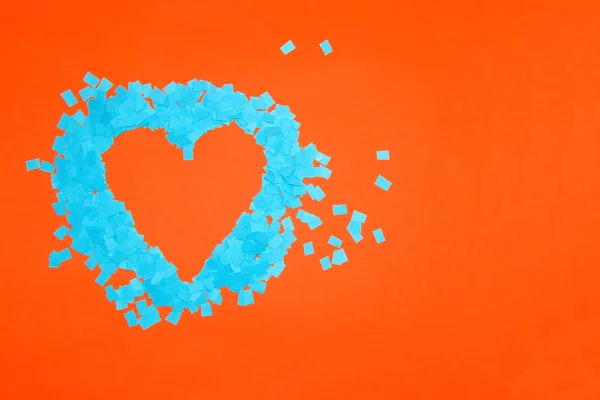 heart frame of blue shredded paper on right side orange background, copy space, art love design with complementary colors