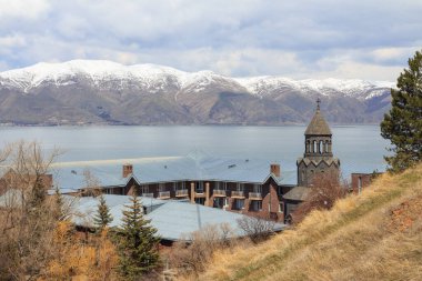 Sevan Gölü yakınlarında karlı dağlara bakan bir yarımada üzerine inşa edilmiş modern manastır manzarası. Ermenistan