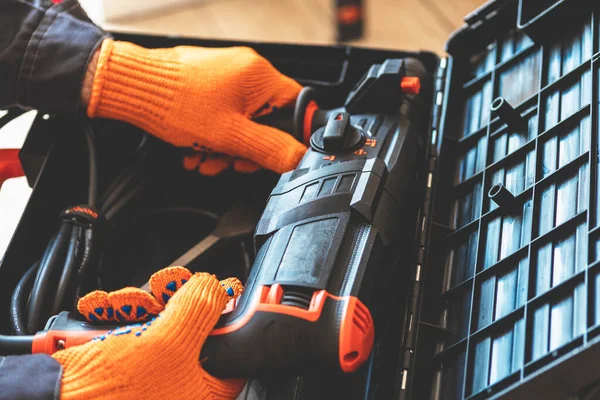 Hands with in protective gloves a rotary hammer close-up. Worker takes hammer drill perforator out of the box.