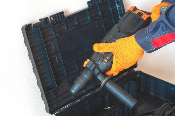 Hands in protective gloves hold  a rotary hammer. worker, professional with hammer drill perforator.