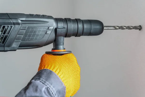 workman hand with a rotary hammer. Hands in protective gloves with hammer drill perforator. close-up