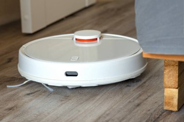 Beyaz robot süpürge yatağın yanında. Ev temizliği konsepti. Ev çöpü. yakın plan