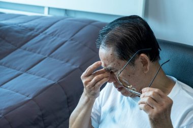 Gözlükleri çıkarın ve ellerinizi tutun, burnunuzun köprüsüne bastırın ve masaj yapın. Kanepedeki yaşlı hastalar, Asyalı kıdemli hastalar baş ağrısı sağlık ve sağlık hizmetleri konsepti