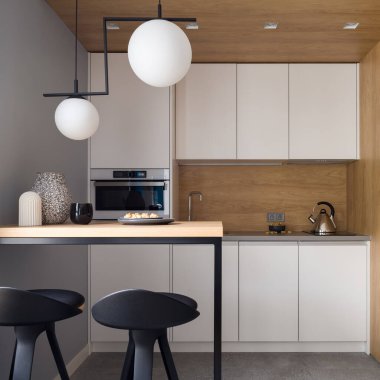 Beyaz mobilyalı küçük ve modern mutfak, şık lambalar, duvarlarında iki sandalye ve ahşap dekor olan masa, tavan ve arka plan