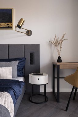 Yatak odasında beyaz komodinli, rahat yataklı ve tahtadan sandalyeli bir masa.