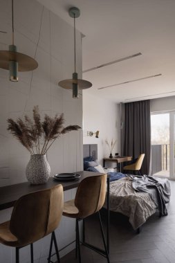 Yatak odasının yanındaki dekoratif lambaların altında iki sarı sandalyeli şık bir masa.