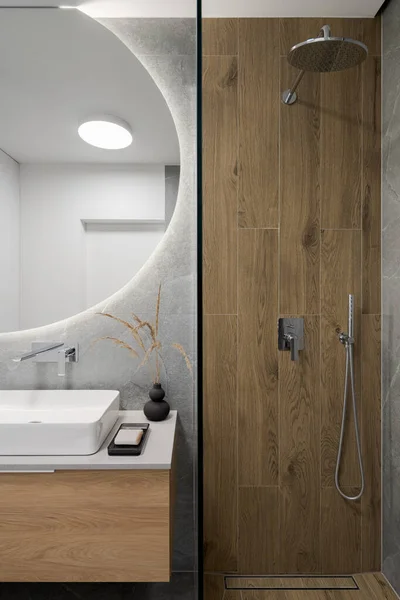 在圆圆的大镜子下 现代化的淋浴房 旁边是时尚的洗脸盆 旁边是木制瓷砖 — 图库照片