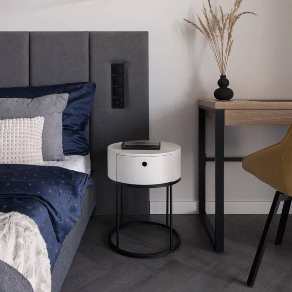 Yatak odasındaki şık ve beyaz komodinli yatak odası ve sandalyeli ahşap masa.