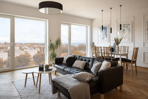 Big windows in spacious living room with black corner sofa and simple dining table