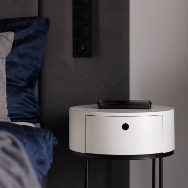 Modern, yuvarlak, siyah beyaz komodinin üzerinde rahat yatağın yanında.