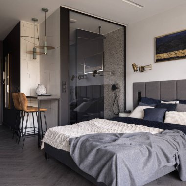 Zarif yatak odası, rahat yatak odası, şık çarşaflar ve cam duvarın arkasında modern duş kabini.