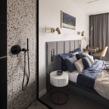 Terrazzo tarzı fayanslı modern duş alanı, siyah musluk ve şık yatak odası ve çalışma odası arasında cam duvar.