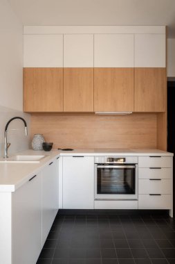 Beyaz ve ahşap mobilyalı, koyu fayanslı basit bir mutfak.
