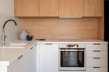 Beyaz dolapları, çekmeceleri ve tezgahları olan basit bir mutfak. Lavabo, fırın ve indüksiyon zulası, ahşap arka sıçrama ve üst dolaplar.