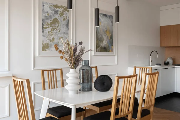 有白色桌子 六张木制椅子和装饰品 现代灯具和简单厨房旁边有趣的艺术的时尚餐厅 — 图库照片
